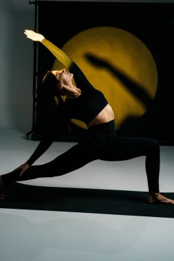 Atletik kadın stüdyoda yoga yapıyor ve arka plandaki ışık aydınlatmalarına karşı poz veriyor. Yoga ve meditasyon konsepti