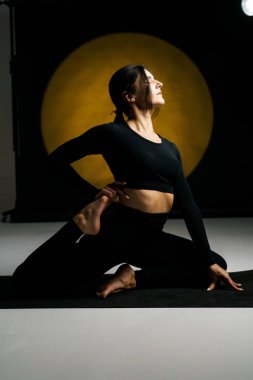 Atletik kadın stüdyoda yoga yapıyor ve arka plandaki ışık aydınlatmalarına karşı poz veriyor. Yoga ve meditasyon konsepti