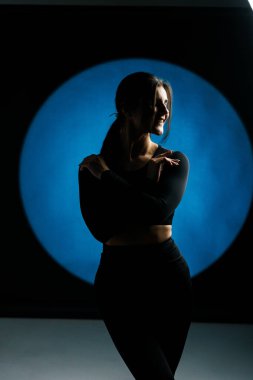 Atletik kadın stüdyoda yoga yapıyor ve arka plandaki ışık aydınlatmalarına karşı poz veriyor. Yoga ve meditasyon konsepti