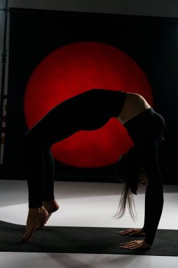 Atletik kadın stüdyoda yoga yapıyor ve arka plandaki ışık aydınlatmalarına karşı poz veriyor. Yoga ve meditasyon konsepti