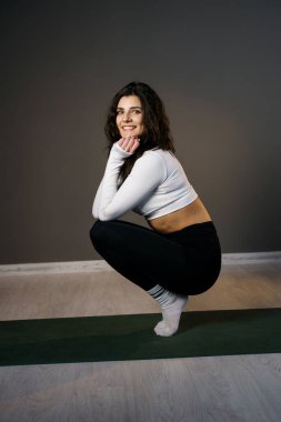 Beyaz spor kıyafetli güzel bir kadın paspasın üzerinde sabah egzersizi yapıyor ve yoga yapıyor.