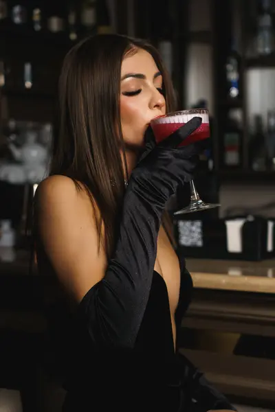 Sexy woman in a black dress with gloves and red lips holds a cocktail.Nightlife concept