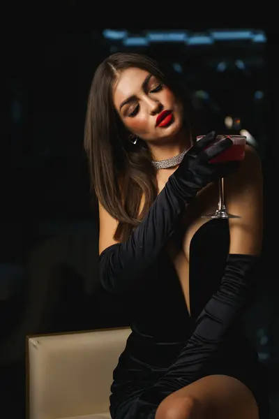 Sexy woman in a black dress with gloves and red lips holds a cocktail.Nightlife concept