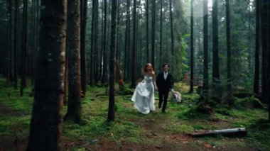 Kızıl saçlı bir gelin, damatla çam ormanında poz veriyor. Peri masalı çifti. Düğün konsepti