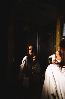 Bornozlu genç bir kadın dudaklarını banyoya boyuyor. Otel tatil konsepti.