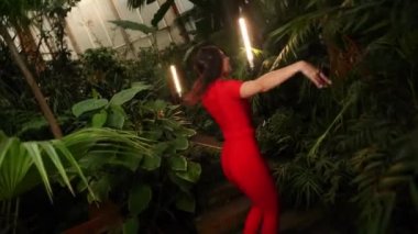 Kırmızı elbiseli hoş bir kadın tropik bir bahçede dans ediyor. Dans konsepti.