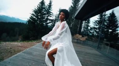 A dark-skinned bride in a white dress poses in the mountains on the terrace. Wedding concept. Portrait of a dark-skinned bride 4k
