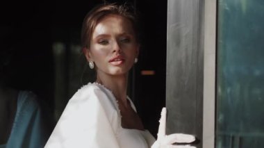 Beyaz eldivenli şık bir kadın model, güneş gören bir pencerenin yanında poz veriyor. Gölgede bir mankenin portresi. Moda çekimi konsepti 4k