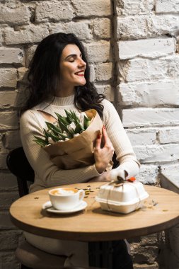 Kahve içip doğum gününü kutlayan mutlu bir kadın. Bir buket lale ve bento kekiyle. Doğum günü hediyesi.