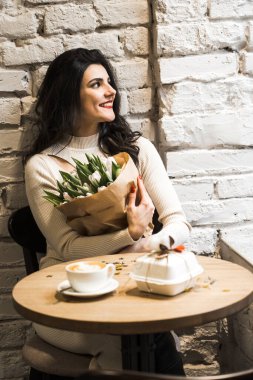 Kahve içip doğum gününü kutlayan mutlu bir kadın. Bir buket lale ve bento kekiyle. Doğum günü hediyesi.