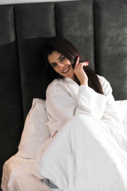 Hoş bir kadın bir otel odasında uyanıyor ve kışın pencereden manzaranın tadını çıkarıyor. Yatakta kahve. Otel tatil konsepti