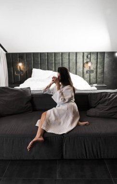 Hoş bir kadın bir otel odasında uyanıyor ve kışın pencereden manzaranın tadını çıkarıyor. Yatakta kahve. Otel tatil konsepti