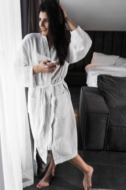 Hoş bir kadın bir otel odasında uyanıyor ve kışın pencereden manzaranın tadını çıkarıyor. Yatakta kahve. Otel tatil konsepti