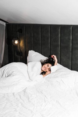 Hoş bir kadın bir otel odasında uyanıyor ve kışın pencereden manzaranın tadını çıkarıyor. Yatakta kahve. Otel tatil konsepti