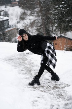 Siyah şapkalı genç bir kadın bir kulübenin yakınındaki karlı dağların arka planında poz veriyor. Kış tatili kavramı