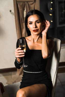 Siyah elbiseli lüks bir kadın, çiçekli ve şampanyalı bir restoranda yemek yiyor. Romantik bir akşam yemeği. Uluslararası Kadınlar Günü konsepti.