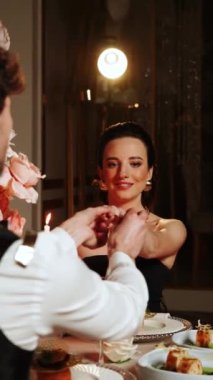 Birbirine aşık bir çiftin romantik yemeği. Bir adam ve bir kadın bir restoranda birlikte akşam yemeği yiyorlar. Adam kıza evlenme teklif etmiş. Kız da evet demiş. Evlilik teklifi konsepti. Dikey video