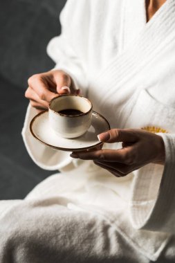 Beyaz bornozlu genç bir kadın ahşap bir otel odasında espresso içiyor. Otel tatili konsepti. Sabah kahvesi