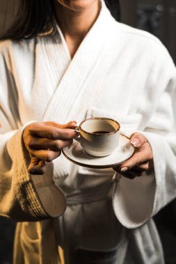 Beyaz bornozlu genç bir kadın ahşap bir otel odasında espresso içiyor. Otel tatili konsepti. Sabah kahvesi