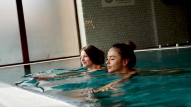 İki seksi kadın havuzda yüzüyor. Kadınlar spa 'da rahatlıyor. Otelde rahatlama konsepti.