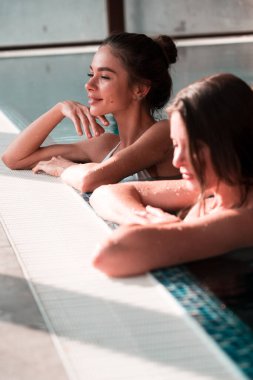 İki seksi kadın havuzda yüzüyor. Kadınlar spa 'da rahatlıyor. Otelde rahatlama konsepti.
