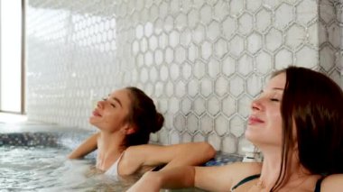 İki seksi kadın şampanya içip jakuzide dinleniyor. Kadın, otel 4K 'deki spa konseptinde rahatlıyor.