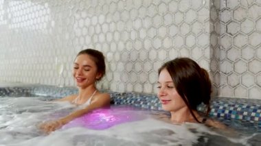 İki seksi kadın şampanya içip jakuzide dinleniyor. Kadın, otel 4K 'deki spa konseptinde rahatlıyor.