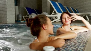 İki seksi kadın şampanya içip jakuzide dinleniyor. Kadın, otel 4K 'deki spa konseptinde rahatlıyor.