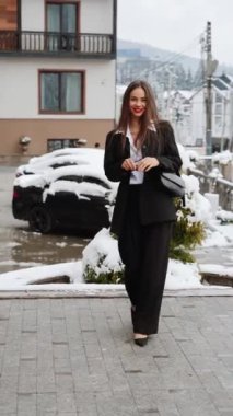 Siyah takım elbiseli, beyaz gömlekli, gözlüklü şık bir kadın karlı dağların arkasında kameraya poz veriyor. Moda çekim konsepti. Dikey video