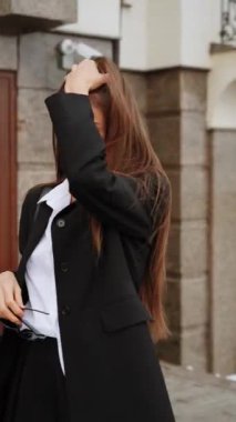 Siyah takım elbiseli, beyaz gömlekli, gözlüklü şık bir kadın karlı dağların arkasında kameraya poz veriyor. Moda çekim konsepti. Dikey video