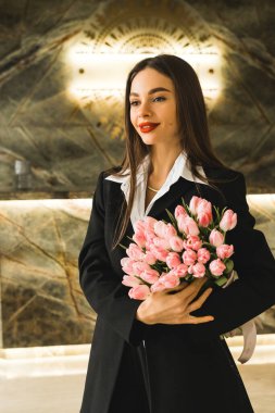 Siyah takım elbiseli güzel bir kadın taze laleler tutuyor. Laleler bir kadının elinde. İş kadını çiçeklere bayılıyor.