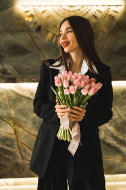 Siyah takım elbiseli güzel bir kadın taze laleler tutuyor. Laleler bir kadının elinde. İş kadını çiçeklere bayılıyor.