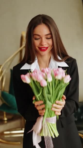 黒いスーツの美しい女性は 新鮮なチューリップの花を保持しています 女性の手でチューリップ ビジネス女性は花に喜んでいます 春の概念 垂直ビデオ — ストック動画