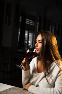 Bir bardak şarap tutan genç bir kadın. Restoranda şarap içen bir kadın. Kırmızı şarap konsepti.