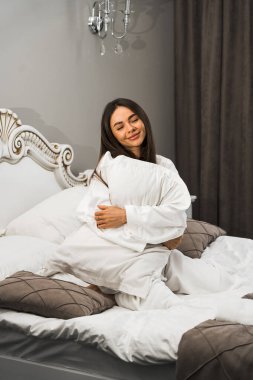 Genç ve güzel bir kadın aydınlık otel odasında uyanıyor. Mutlu bir kadının sabahı. Otel tatil konsepti.