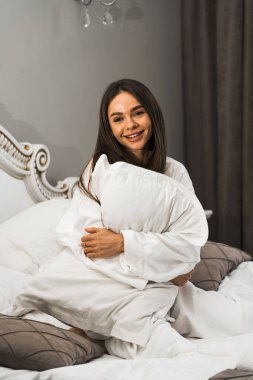 Genç ve güzel bir kadın aydınlık otel odasında uyanıyor. Mutlu bir kadının sabahı. Otel tatil konsepti.
