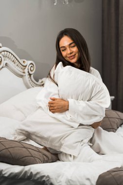 Genç ve güzel bir kadın aydınlık otel odasında uyanıyor. Mutlu bir kadının sabahı. Otel tatil konsepti.