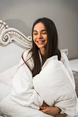 Genç ve güzel bir kadın aydınlık otel odasında uyanıyor. Mutlu bir kadının sabahı. Otel tatil konsepti.