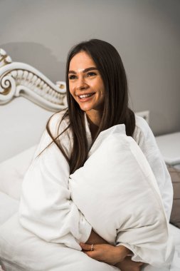 Genç ve güzel bir kadın aydınlık otel odasında uyanıyor. Mutlu bir kadının sabahı. Otel tatil konsepti.