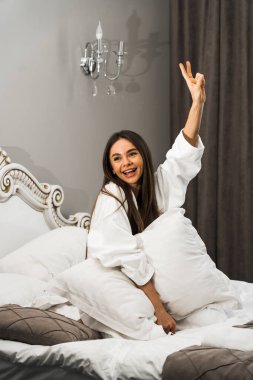 Genç ve güzel bir kadın aydınlık otel odasında uyanıyor. Mutlu bir kadının sabahı. Otel tatil konsepti.