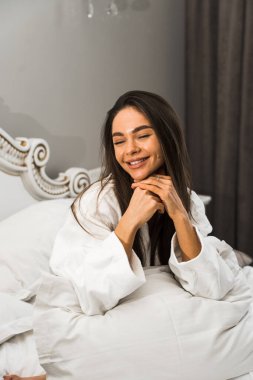 Genç ve güzel bir kadın aydınlık otel odasında uyanıyor. Mutlu bir kadının sabahı. Otel tatil konsepti.