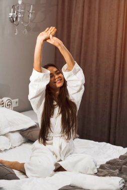Genç ve güzel bir kadın aydınlık otel odasında uyanıyor. Mutlu bir kadının sabahı. Otel tatil konsepti.