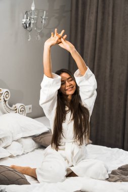 Genç ve güzel bir kadın aydınlık otel odasında uyanıyor. Mutlu bir kadının sabahı. Otel tatil konsepti.