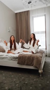 Sabahları yatakta meditasyon yapan iki genç kadın. Meditasyon ve yoga konsepti. Dikey video.