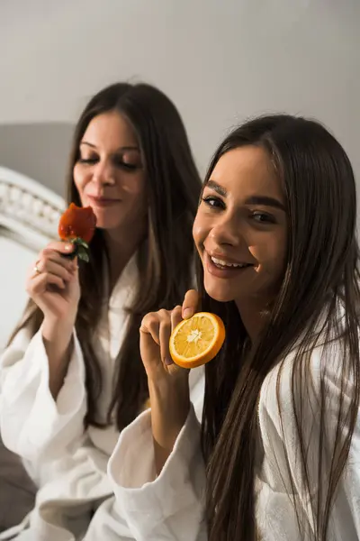 Young women in bathrobes have breakfast in bed, drink coffee and fool around. Breakfast cheesecakes and fruits with coffee. Hotel holiday concept