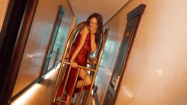 赤いドレスの2人のセクシーな女性は ホテルで黄金の荷物トロリーに乗ります ファッションシューティングコンセプト — ストック動画