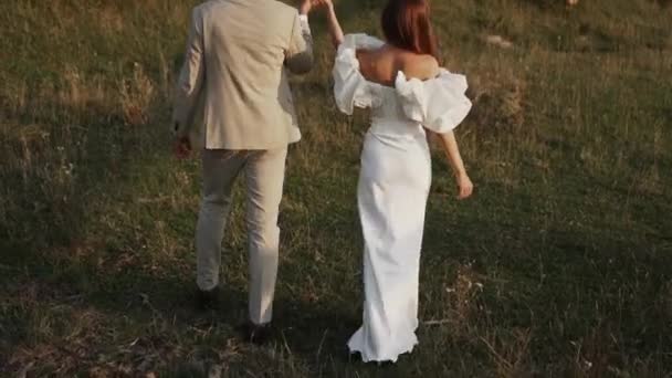 Menyasszony Vőlegény Sétálnak Napnyugtakor Gyönyörű Mezők Dombok Nevetni Táncolni Esküvőnapi — Stock videók