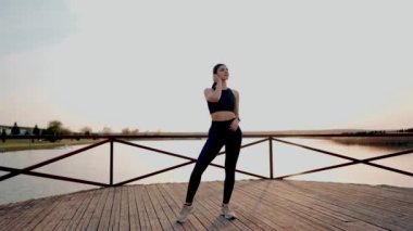 Gün batımında gölün yanındaki parkta spor yapan genç atletik kadın. Hayat konsepti.