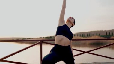 Gün batımında gölün yanındaki parkta spor yapan genç atletik kadın. Hayat konsepti.