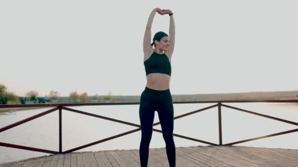 日没の湖近くの公園でフィットネスエクササイズをしている若い運動女性 スポーツライフコンセプト — ストック動画
